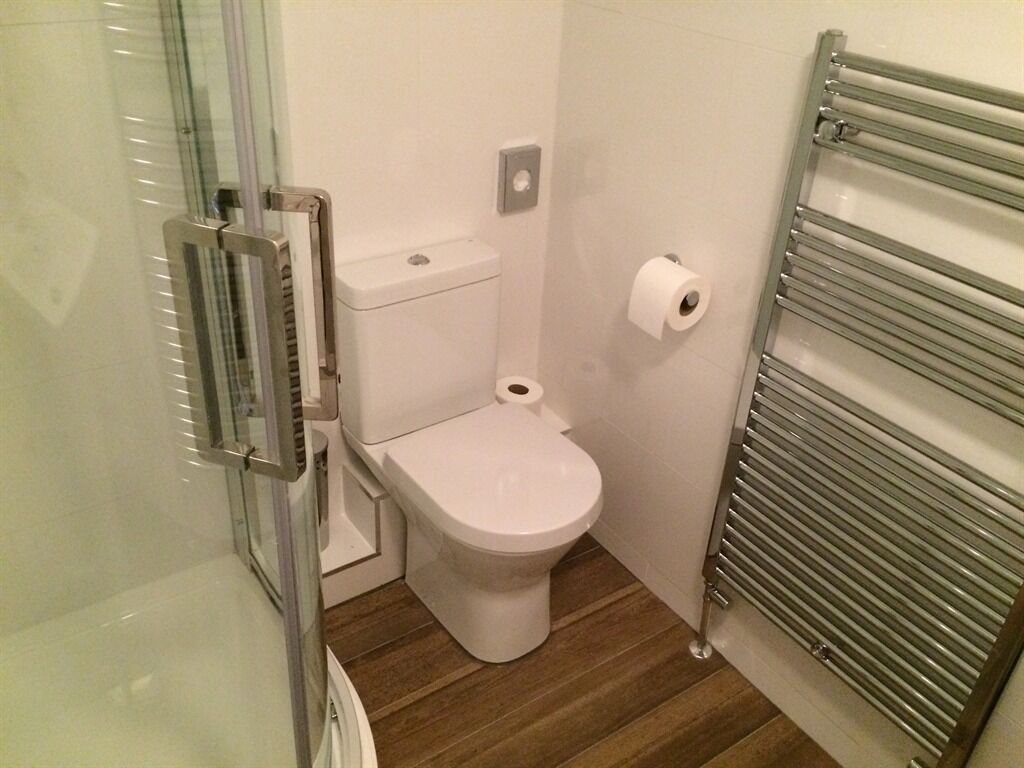 Un baño pequeño con cabina de ducha de vidrio, inodoro y perchero para toallas.