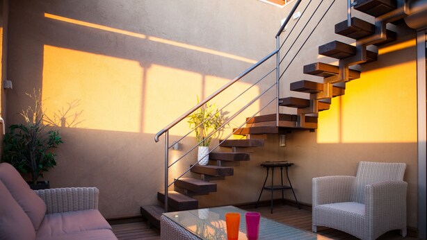 A modern outdoor living area with a glass-top table, wicker furniture, and a staircase. - Sea View High End Rooftop Triplex (Tel Aviv)