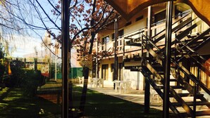 Vista a través de una ventana que muestra un edificio con escaleras, asientos exteriores y una zona verde.