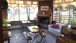 Un cuarto acogedor con chimenea, mesas de madera, bancos y un sofá blanco.