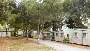 A row of mobile homes with green roofs and white walls, surrounded by trees. - Camping As Cancelas (Santiago de Compostela)