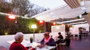 An outdoor patio area with tables and chairs, surrounded by a white canopy and greenery. - Camping As Cancelas (Santiago de Compostela)
