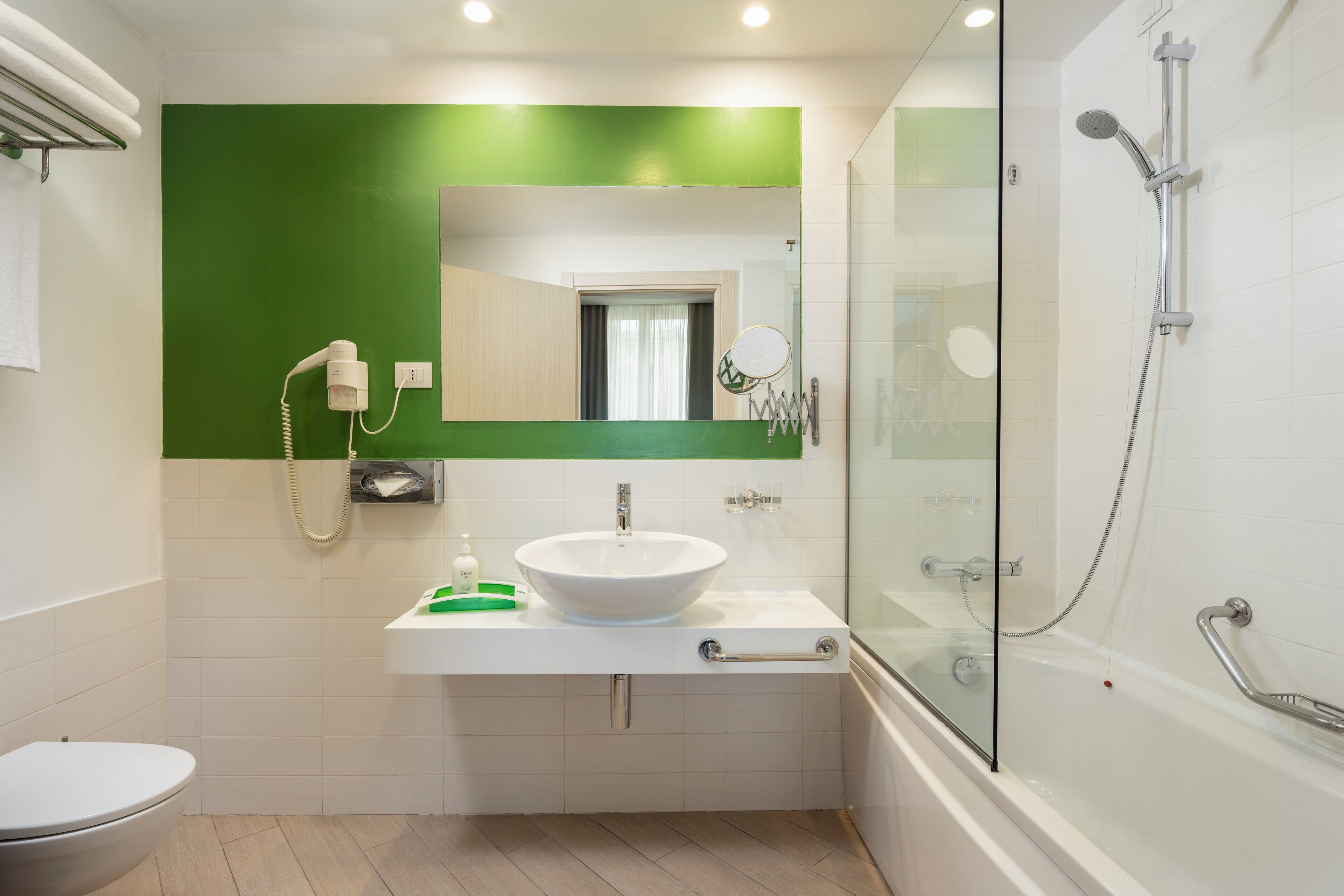 Une salle de bain moderne avec un lavabo blanc, un mur d’accent vert et une douche séparée par des parois en verre.