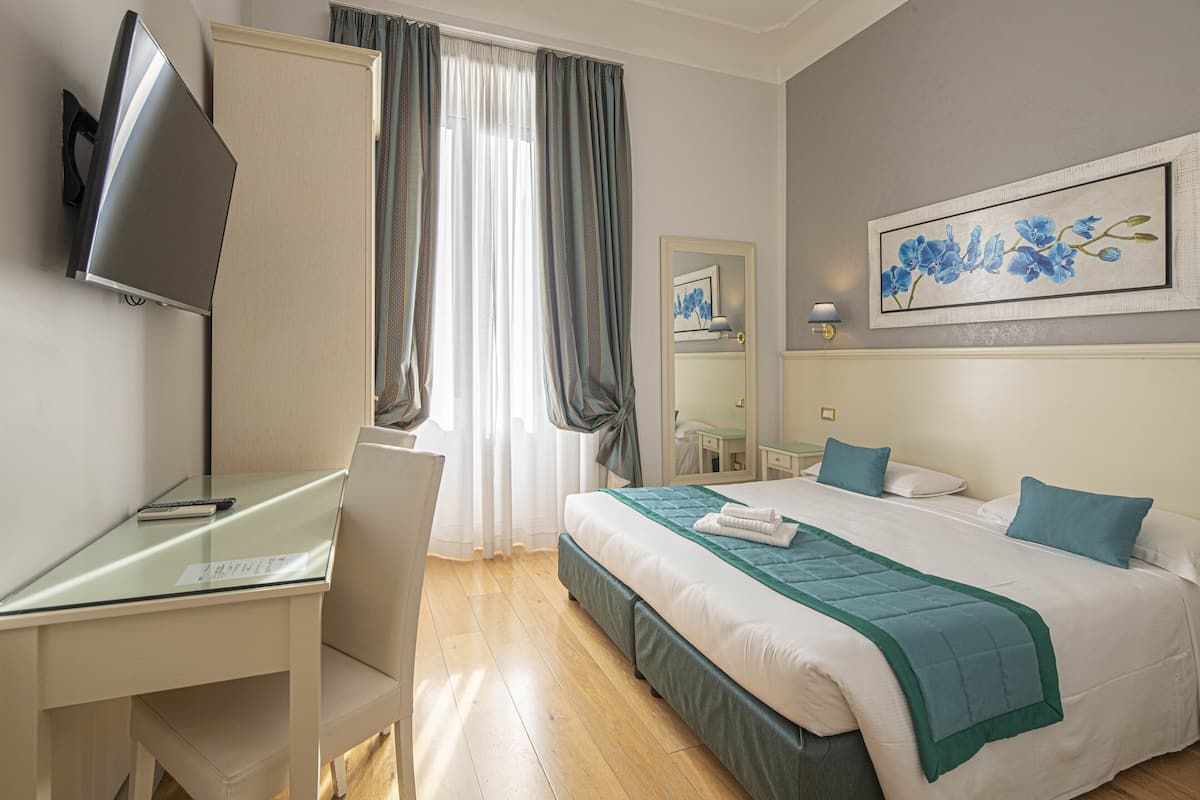 A hotel room with a bed, a desk with a chair, a television, and a painting on the wall.