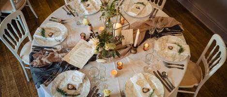 A round table set for a formal dinner with white chairs, candles, and floral centerpieces.
