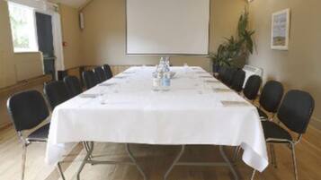 A conference room with a long table, chairs, a projector screen, and a plant.