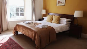 A neatly made bed with a brown bedspread and white pillows, two bedside lamps, a window with curtains, and a framed picture on the wall.