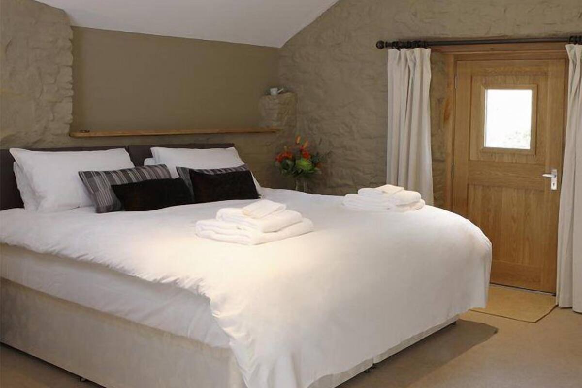 Uma cama bem arrumada com lençóis e almofadas brancos, uma porta de madeira e uma parede de pedra.