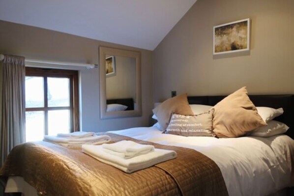 Une chambre d’hôtel avec un lit, une fenêtre avec des rideaux, un miroir et un tableau au mur.