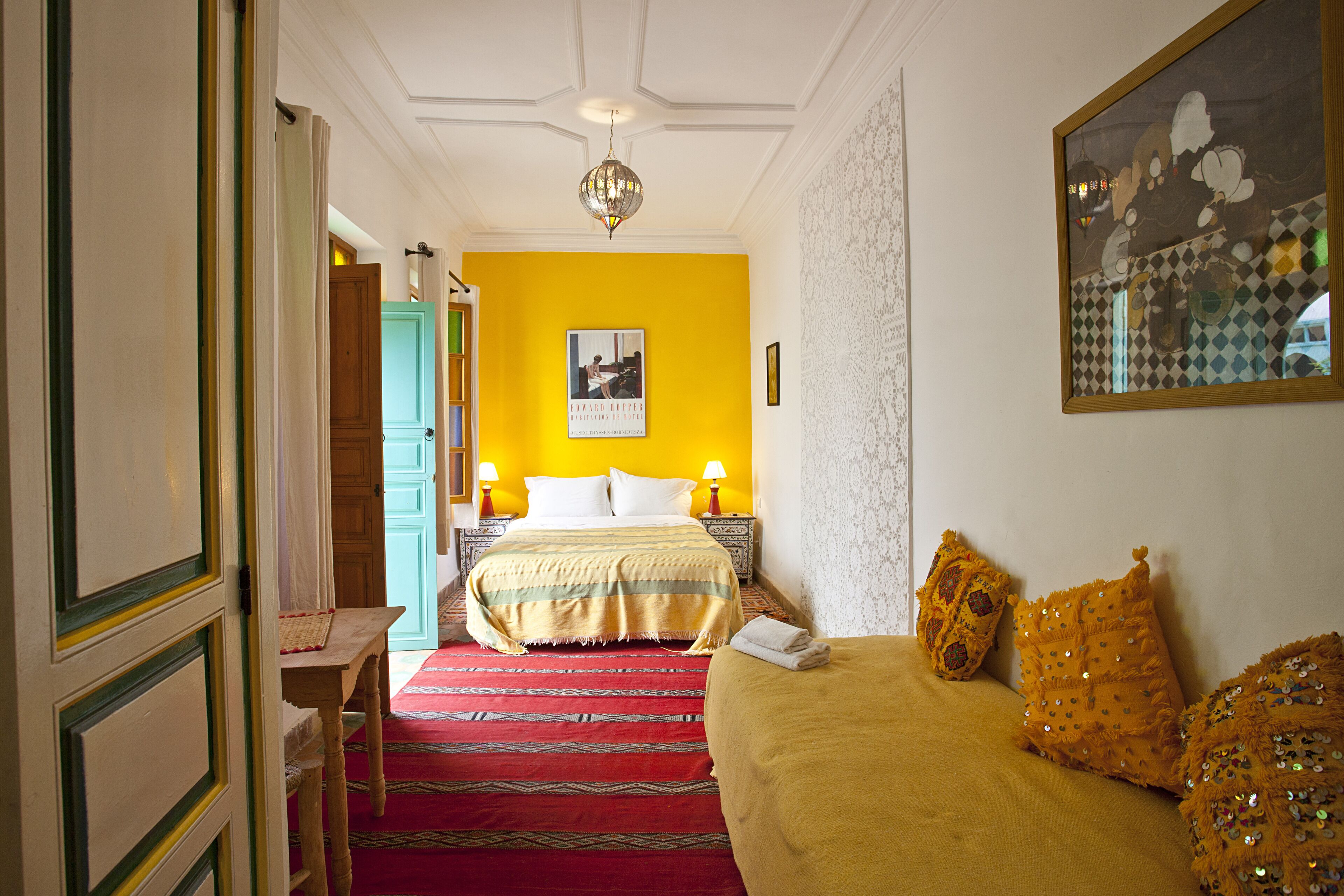 Une chambre d’hôtel avec un lit, un canapé, une moquette rouge et un tableau au mur.