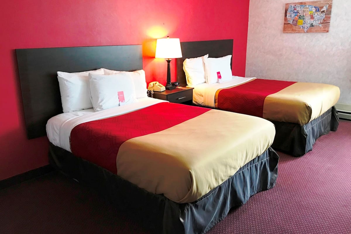 A hotel room with two beds, red walls, and a nightstand with a lamp.