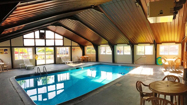 Une piscine intérieure à l’eau claire, entourée de chaises longues et de tables, et dotée de grandes fenêtres laissant entrer la lumière naturelle.