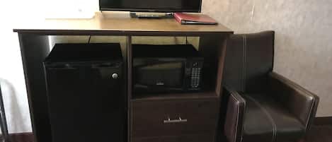 Ett kompakt hotellrum med ett skrivbord i trä, en platt-TV, en mikrovågsugn och ett litet arkivskåp. En läderstol står placerad bredvid skrivbordet.
