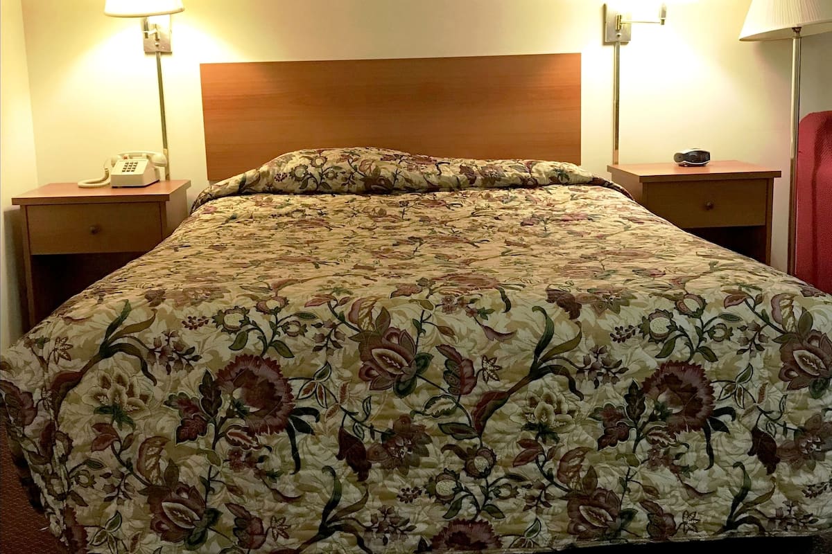 A hotel room with a floral-patterned bedspread, wooden headboard, two bedside tables with lamps, and a telephone on the left table.