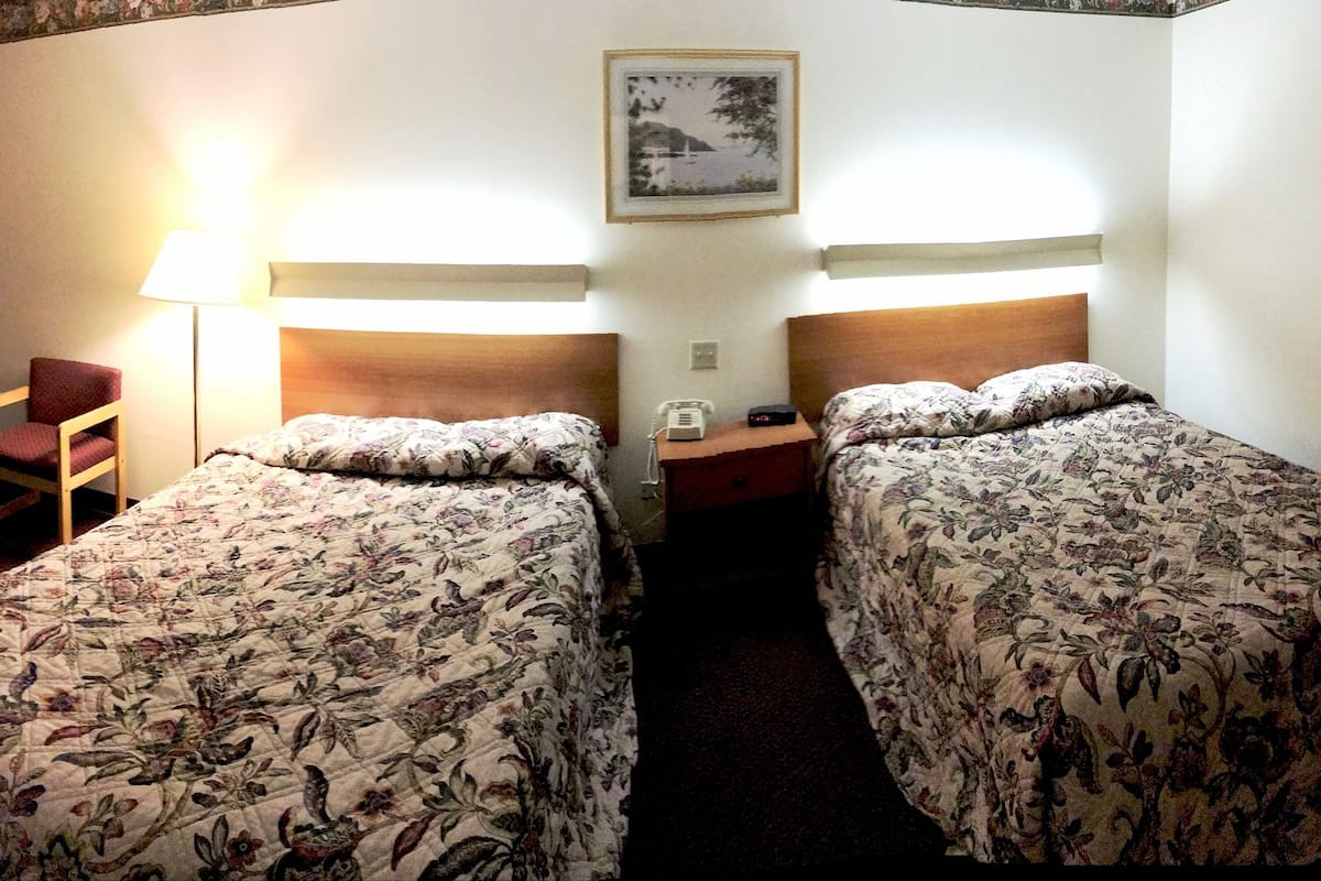 A hotel room with two single beds, a desk with a chair, a microwave, a telephone, and a picture on the wall.