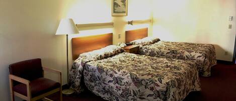 A hotel room with a double bed, a chair, a lamp, and a framed picture on the wall.