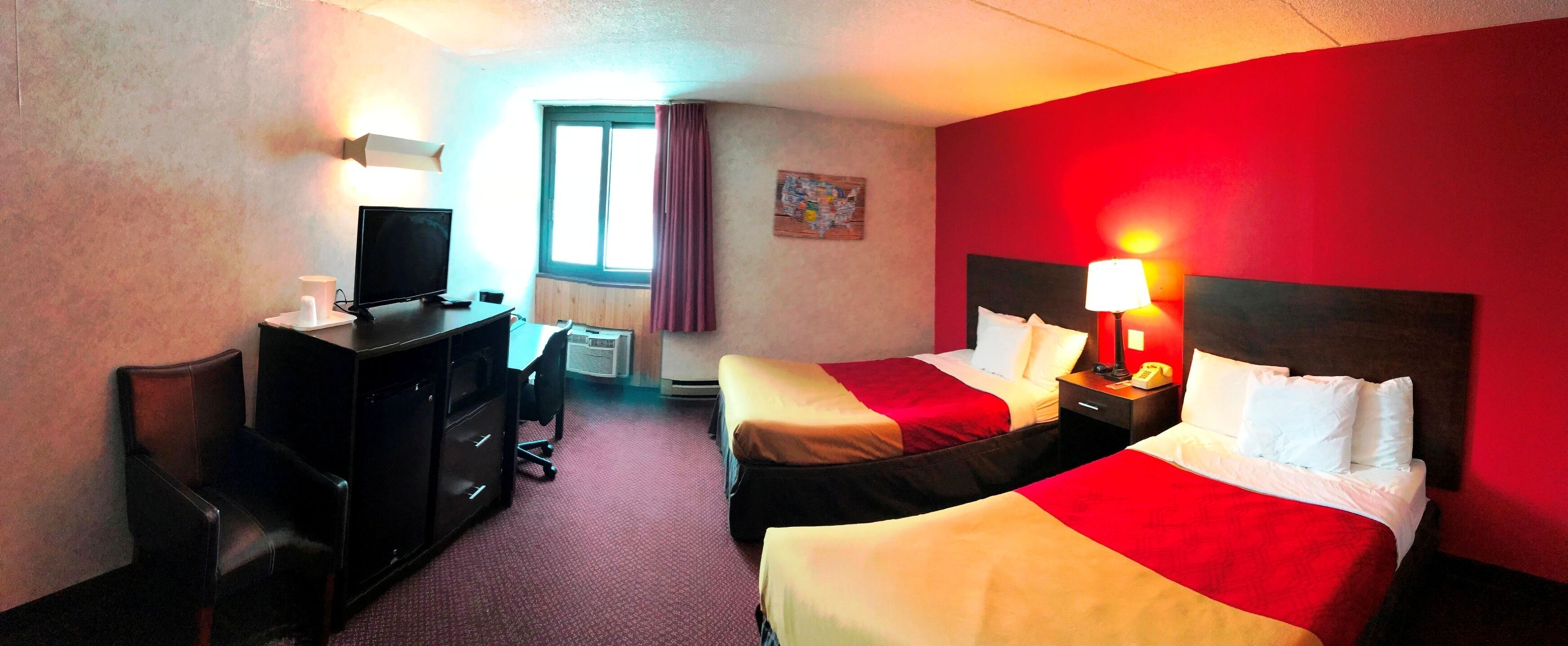 A hotel room with two beds, a desk with a computer, a TV, and a window with curtains.