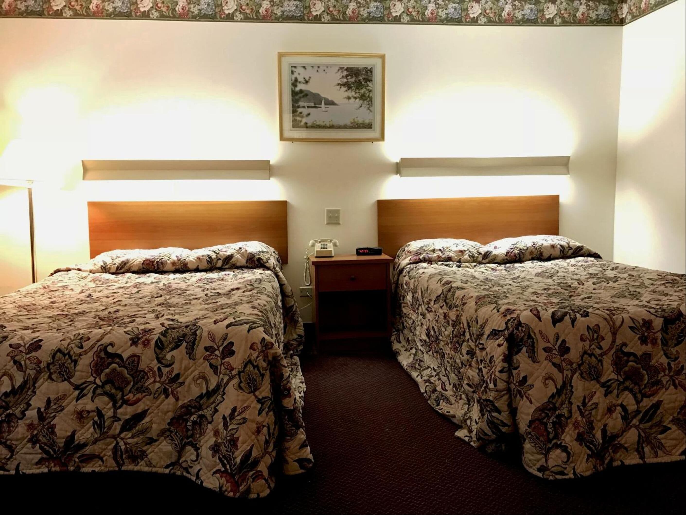 Een hotelkamer met twee bedden, elk voorzien van bloemenprint beddengoed, een nachtkastje met telefoon, en een schilderij aan de muur.