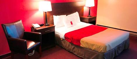 A hotel room with a bed, two bedside tables, a chair, and a red carpet.