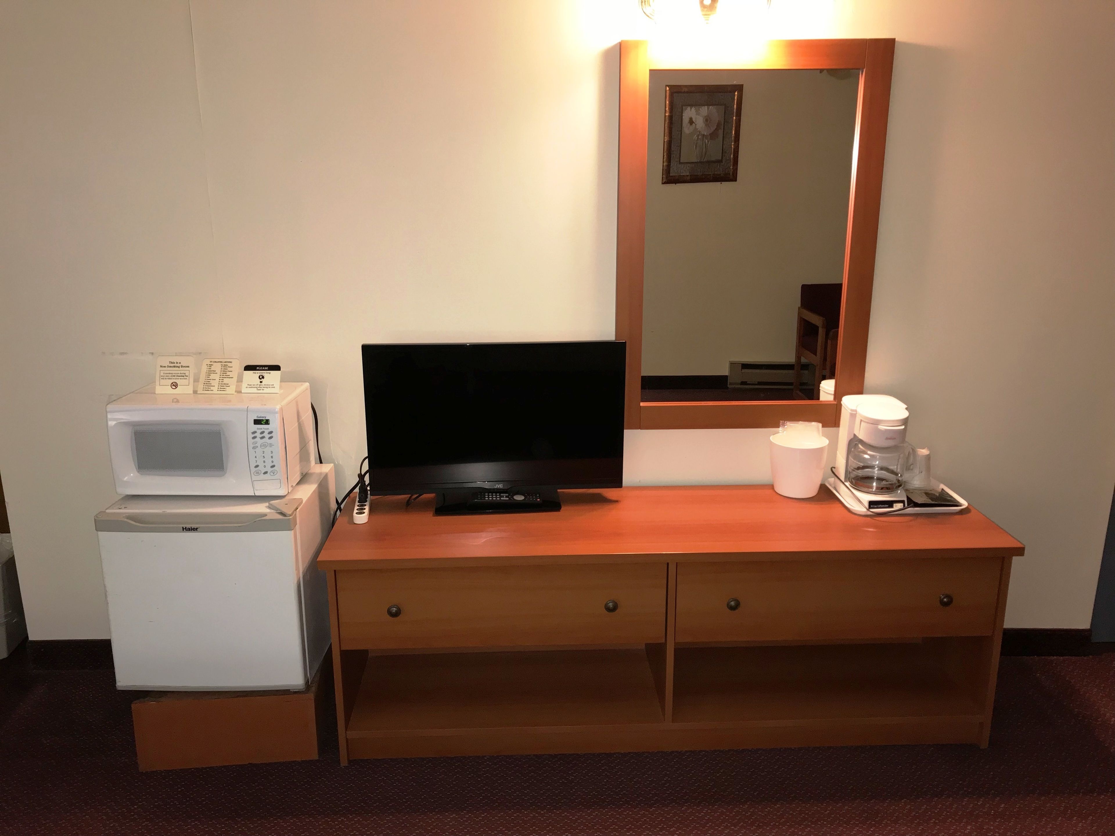 Ett hotellrum med ett skrivbord i trä, en tv, en mikrovågsugn, en kaffebryggare och ett litet kylskåp.