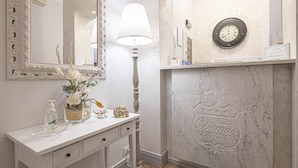 A bathroom with a white vanity, a mirror, a wall clock, and a decorative fireplace with the brand name 'Domini Gastrense'. - Residenza Castrense (Rome)