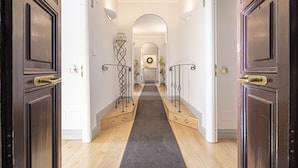 A hallway with wooden floors, dark wooden doors, and a central archway leading to another room. - Residenza Castrense (Rome)