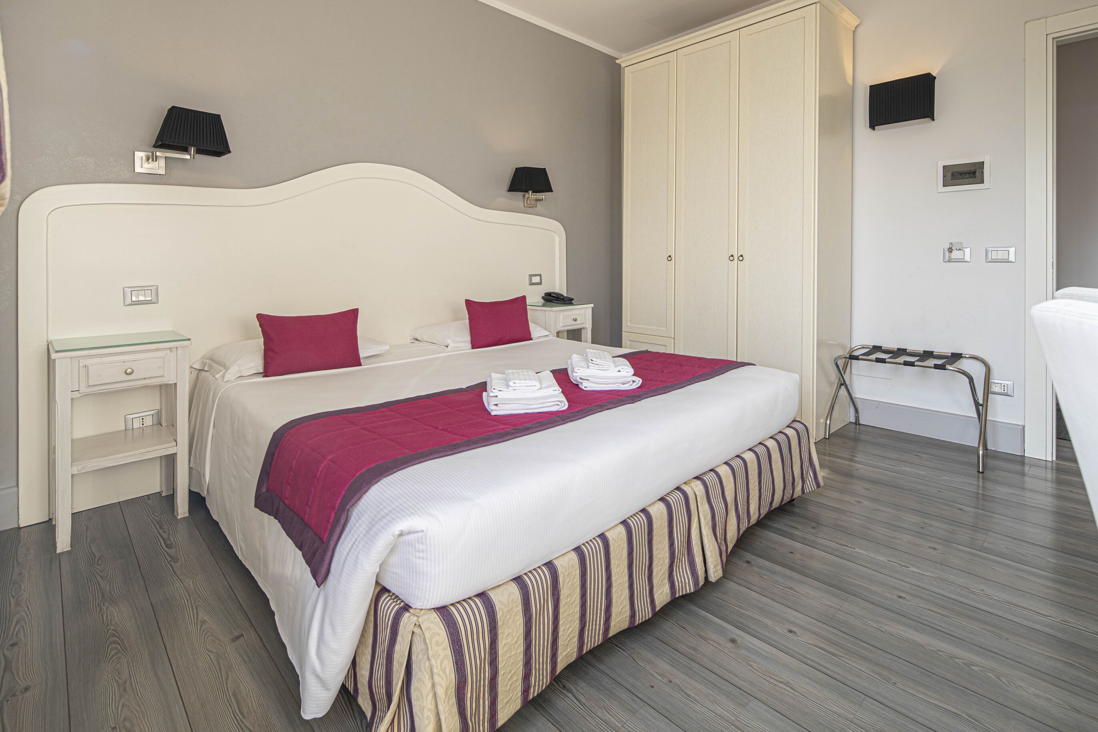 A neatly arranged bedroom with a large bed, bedside tables, a wardrobe, and a small seating area.