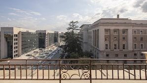 A view from a balcony with a metal railing, overlooking a city street with buildings, a tree, and a clear sky. - Residenza Castrense (Rome)