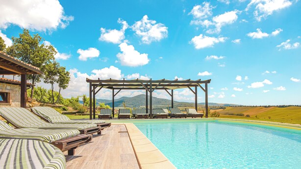 Zona de piscina con sillones de descanso y una pérgola.