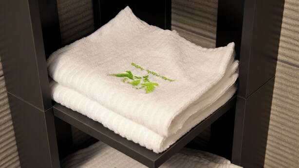 A stack of white towels with green leaf patterns on a dark wooden shelf. - Casale Poggio Nebbia (Tarquinia)