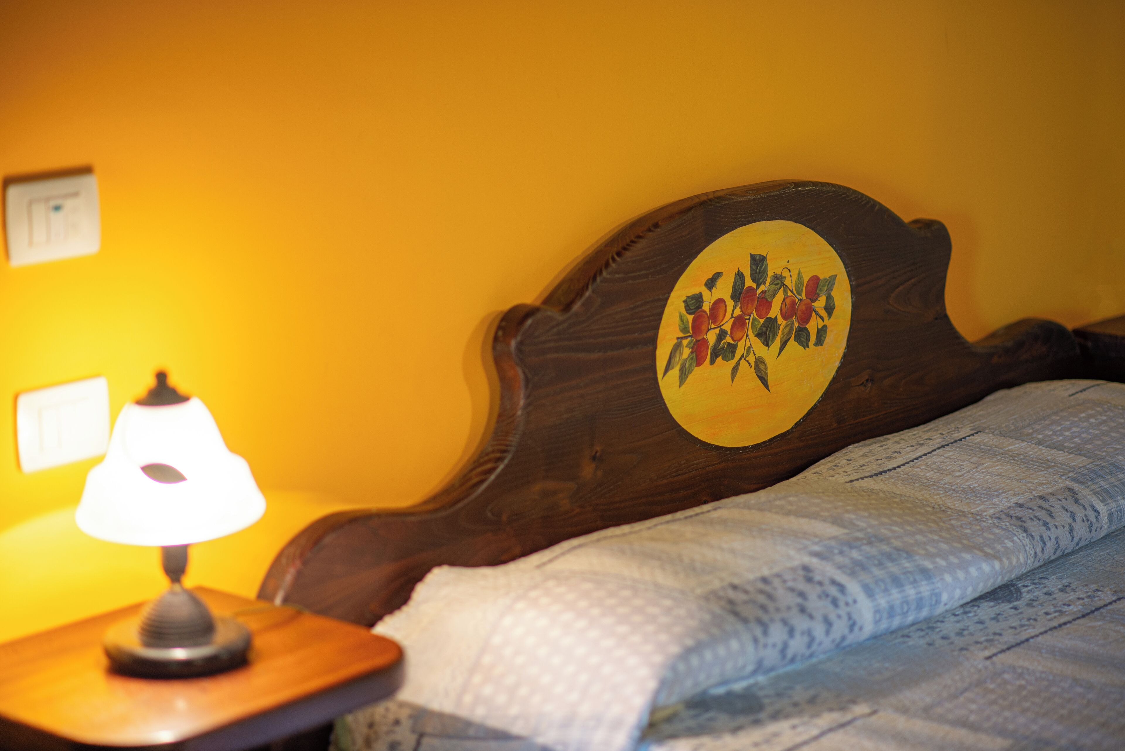 A wooden bed with a circular headboard featuring a painted design, a bedside lamp, and a quilted blanket.