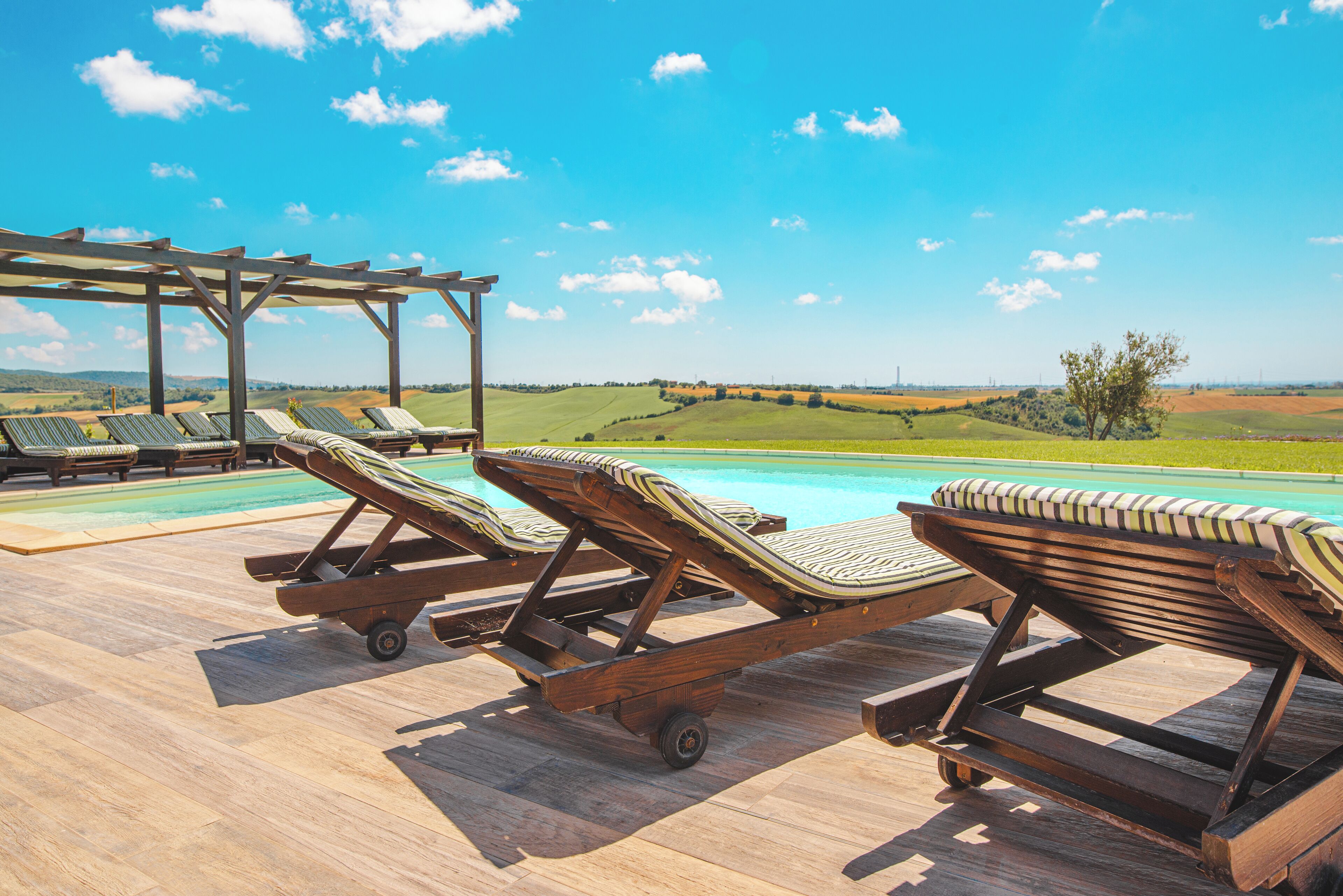 A poolside area with wooden lounge chairs and a pergola overlooking a scenic landscape.