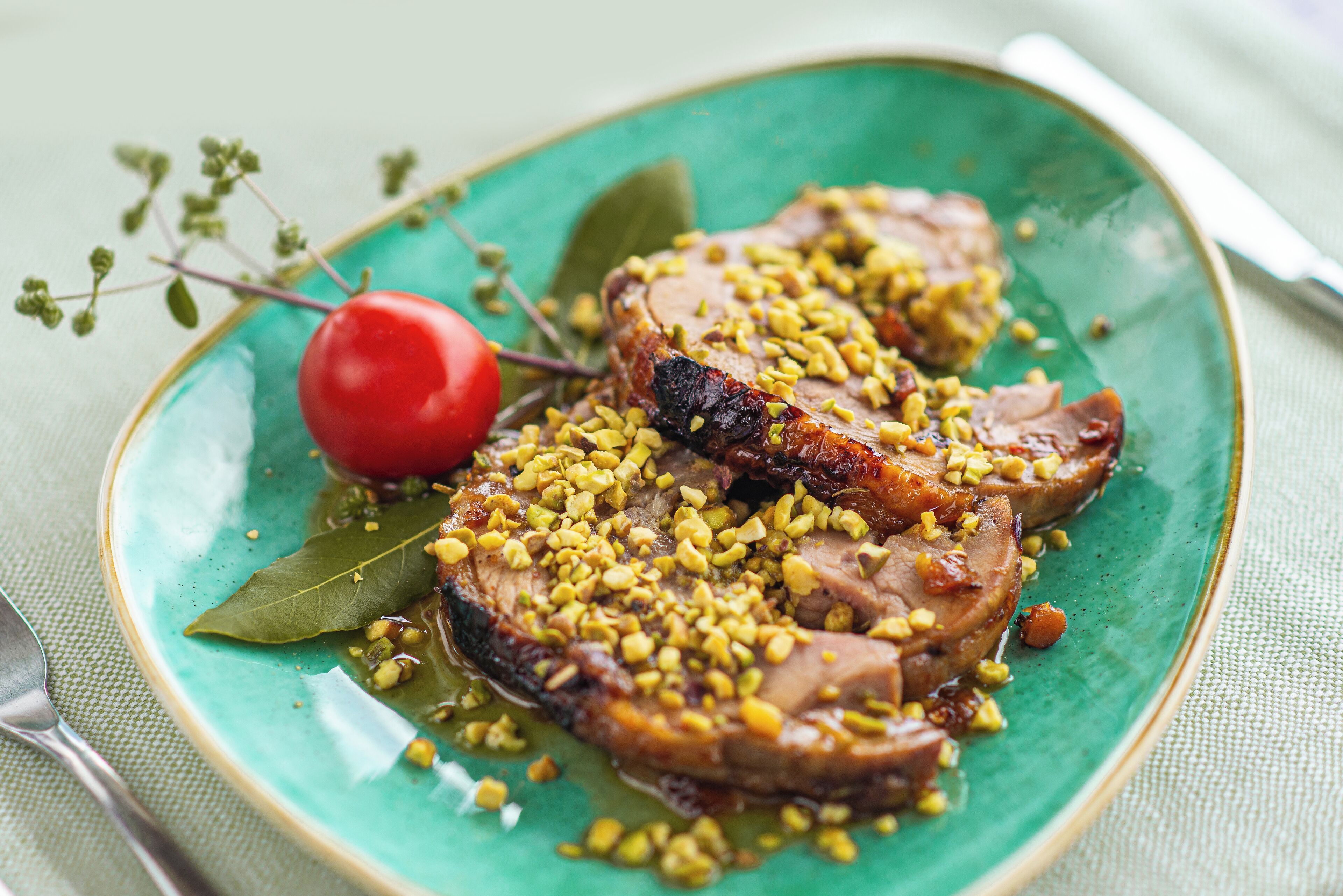 A plate with sliced meat, garnished with corn kernels and a cherry, on a green plate with a bay leaf.