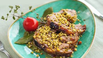 A plate with sliced meat, garnished with corn kernels and a cherry, on a green plate with a bay leaf.