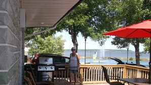 Una terraza de madera con una parrilla, asientos al aire libre y vista a un lago.