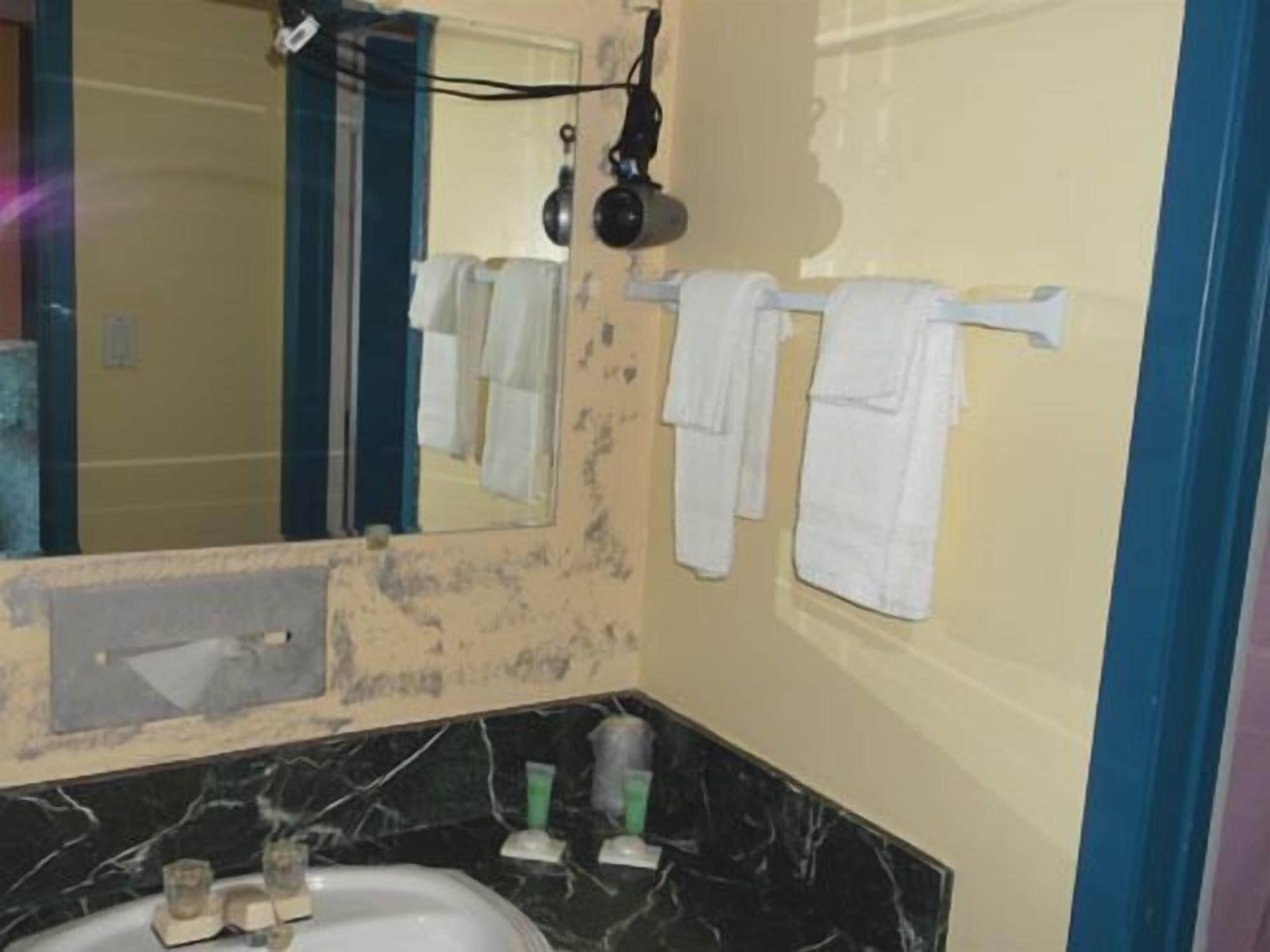 A bathroom with a sink, mirror, towel rack, and a damaged wall.