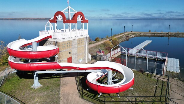 Una estructura de tobogán de agua con diseño rojo y blanco, una plataforma de observación y vistas claras del cuerpo de agua circundante.