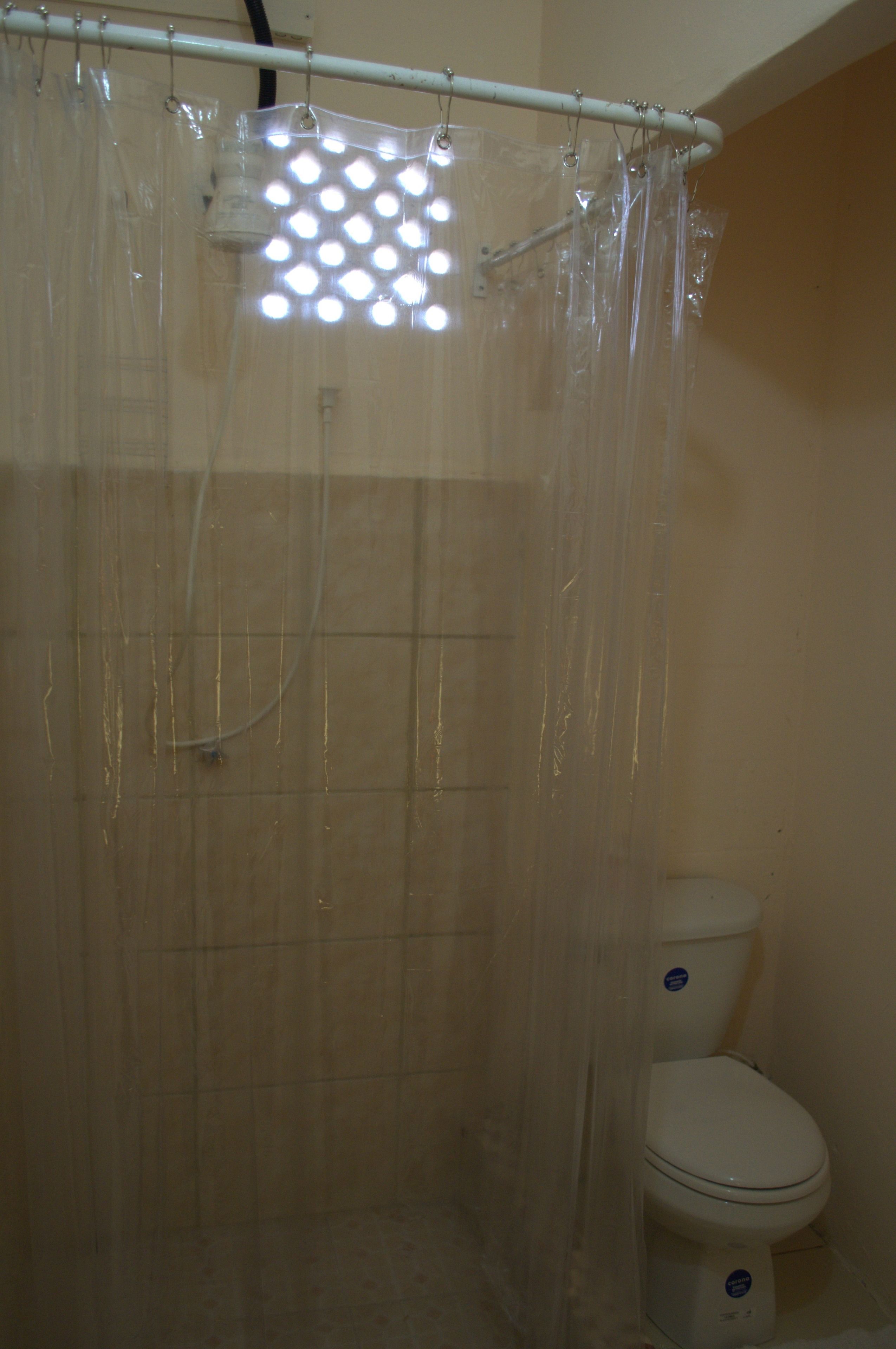 A bathroom with a shower curtain, a toilet, and a visible showerhead.