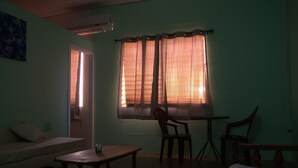 A room with a bed, a small table, a chair, and a desk. There is a window with curtains, and an air conditioning unit on the wall. - Port Lodge (Port of Spain)