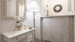 A bathroom with a white vanity, a mirror, a wall clock, and a decorative fireplace with the brand name 'Domini Gastrense'. - Suite Castrense (Rome)