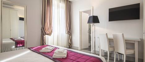 Une chambre d’hôtel avec un lit, un bureau, deux chaises, une télévision et une porte de salle de bain.