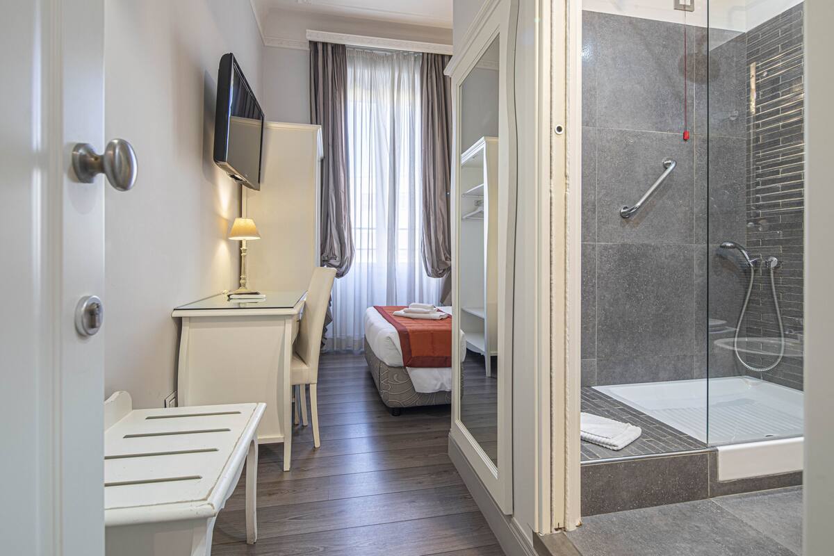 Una habitación de hotel con ducha, cama, escritorio y televisor.