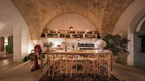 Um salão abobadado de pedra com uma mesa e cadeiras de madeira, uma estante para vinhos e um globo.