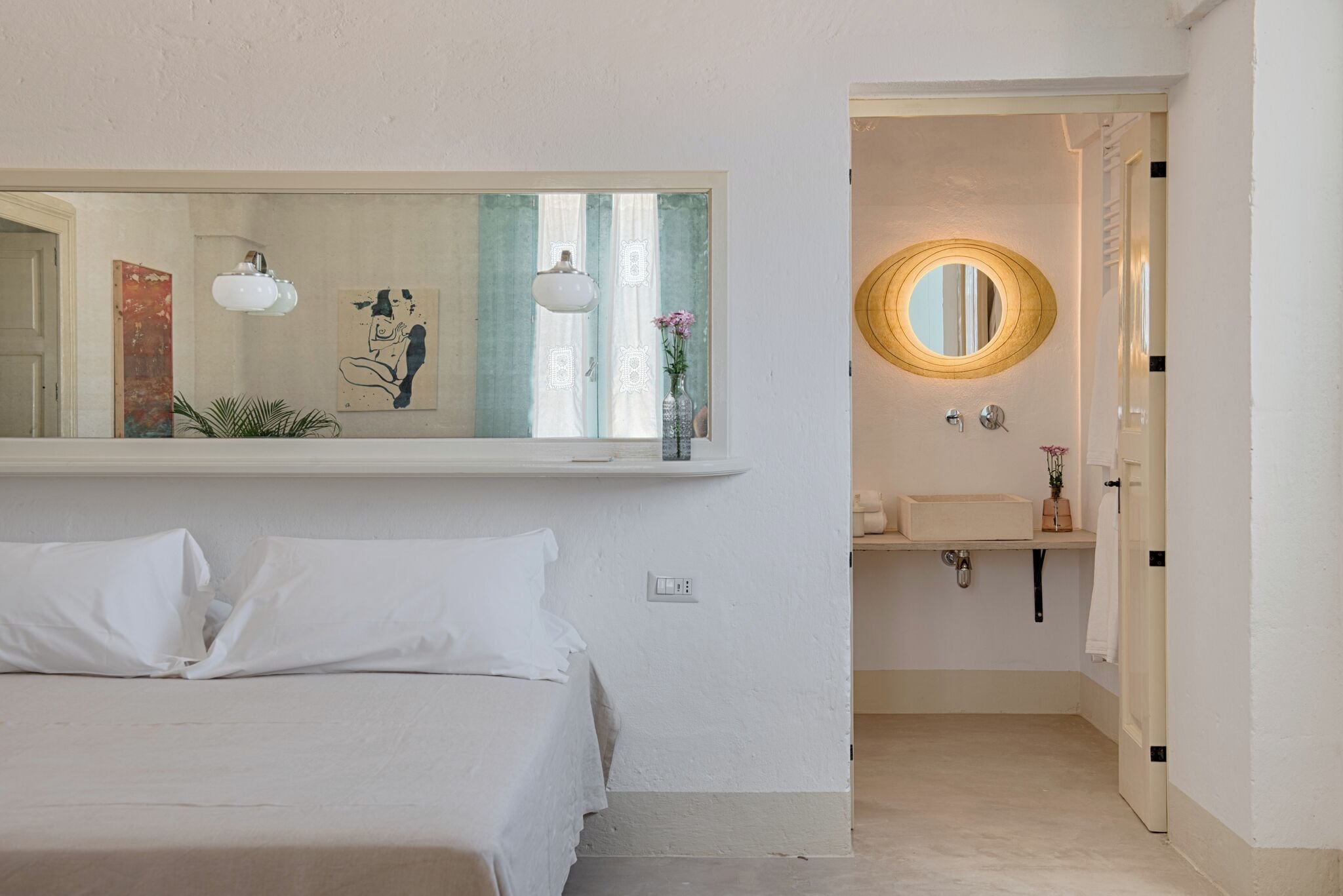 A bedroom with a bed, a bedside table, a mirror, and a wall-mounted shelf with a vase and a plant.