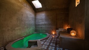 Um quarto de spa com banheira de hidromassagem verde, piso ladrilhado e velas.