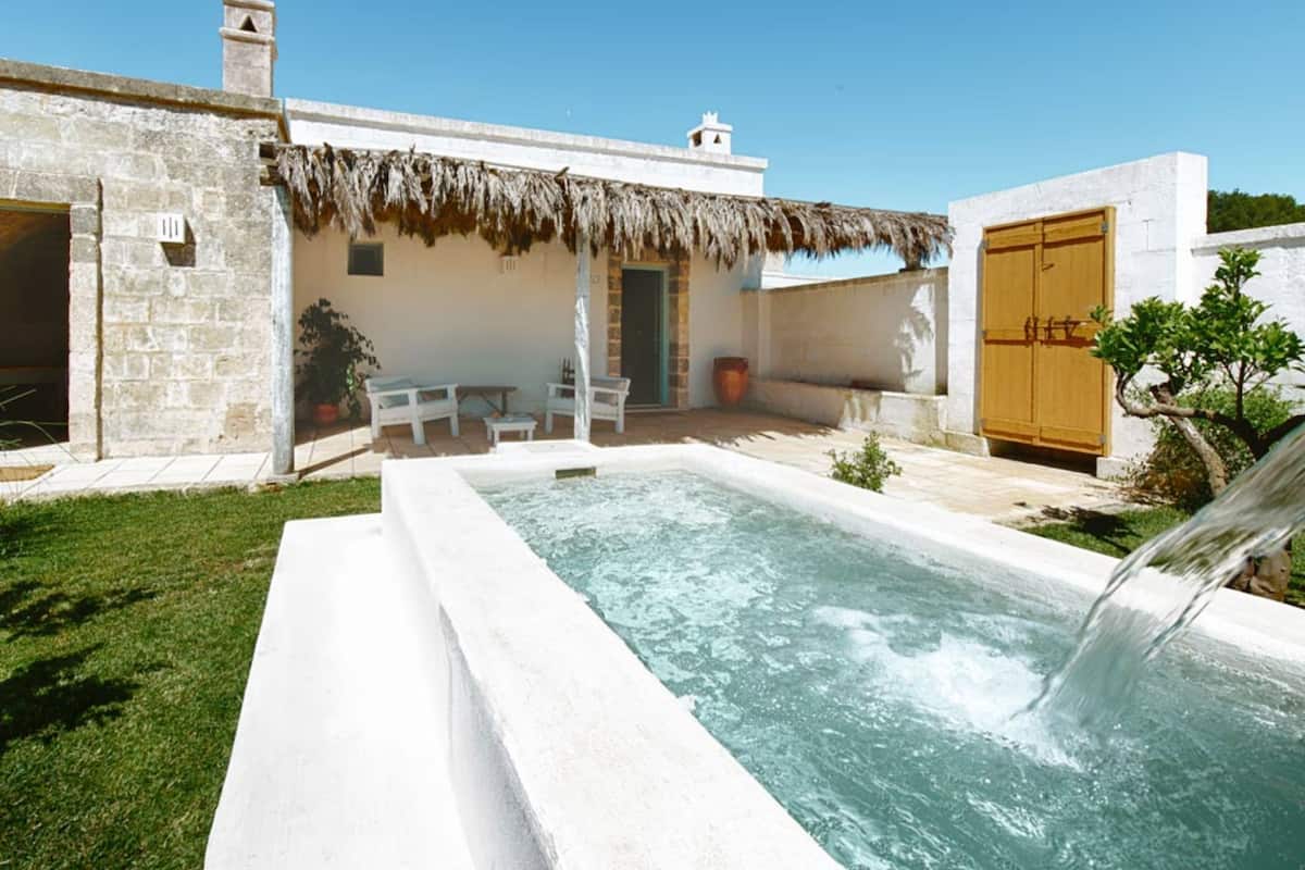 A pool with a waterfall feature, a thatched-roof structure, and a wooden door.