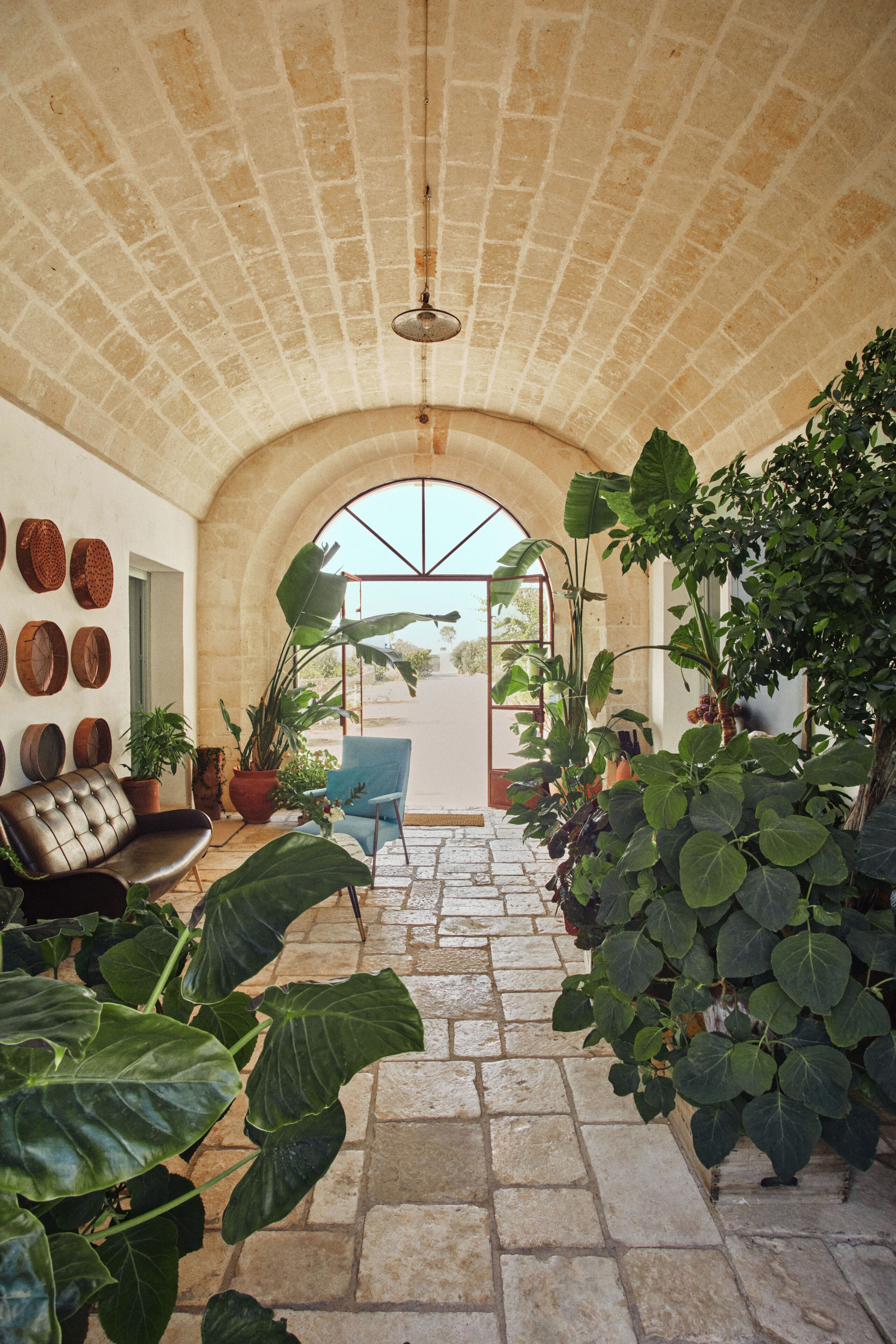 An indoor corridor with a stone floor, a leather sofa, potted plants, and a blue chair.