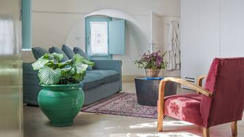 Ein Wohnzimmer mit einer Couch, einem roten Sessel, einer Zimmerpflanze und einem Fenster mit blauen Lamellen.
