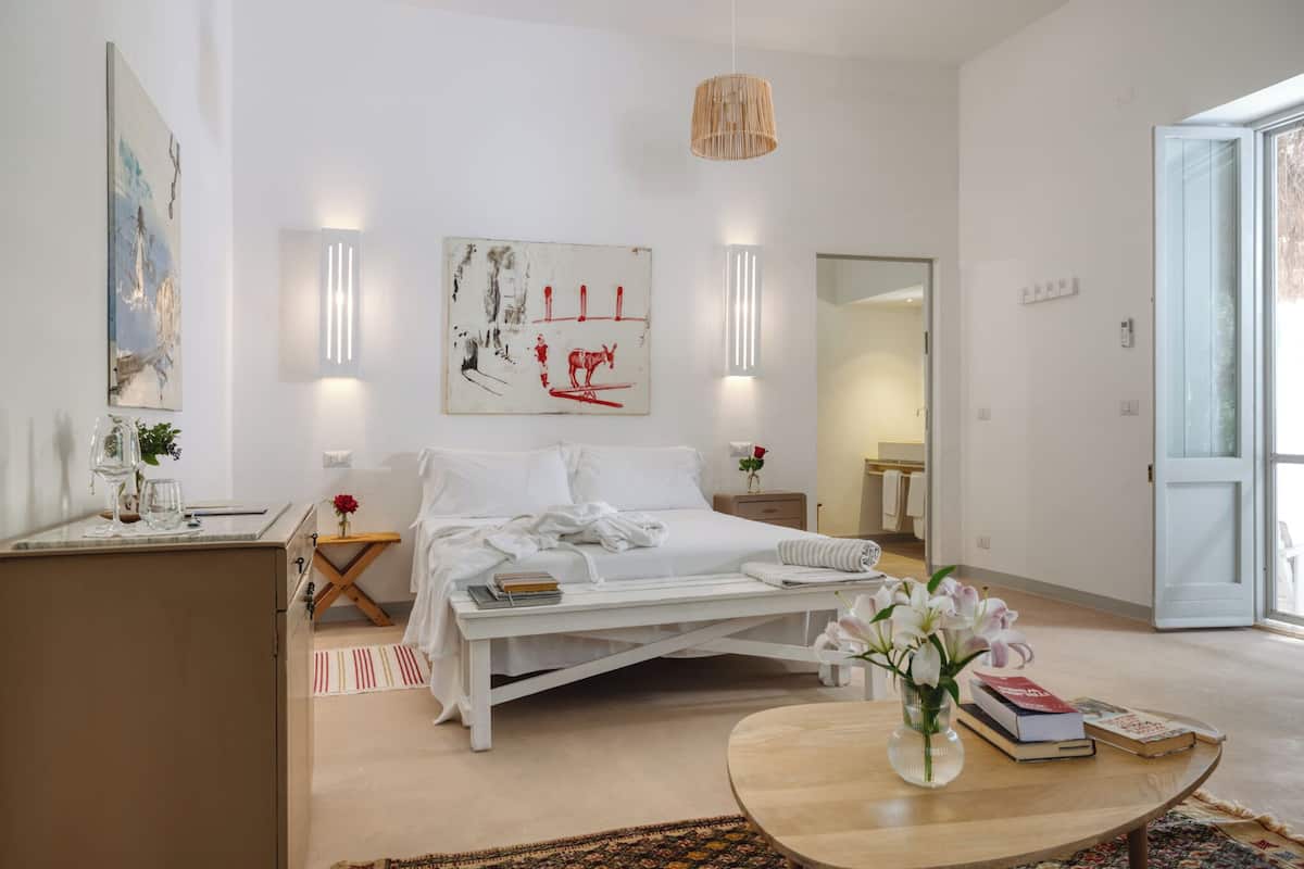 A modern bedroom with a bed, bedside table, and a round coffee table with books and flowers.