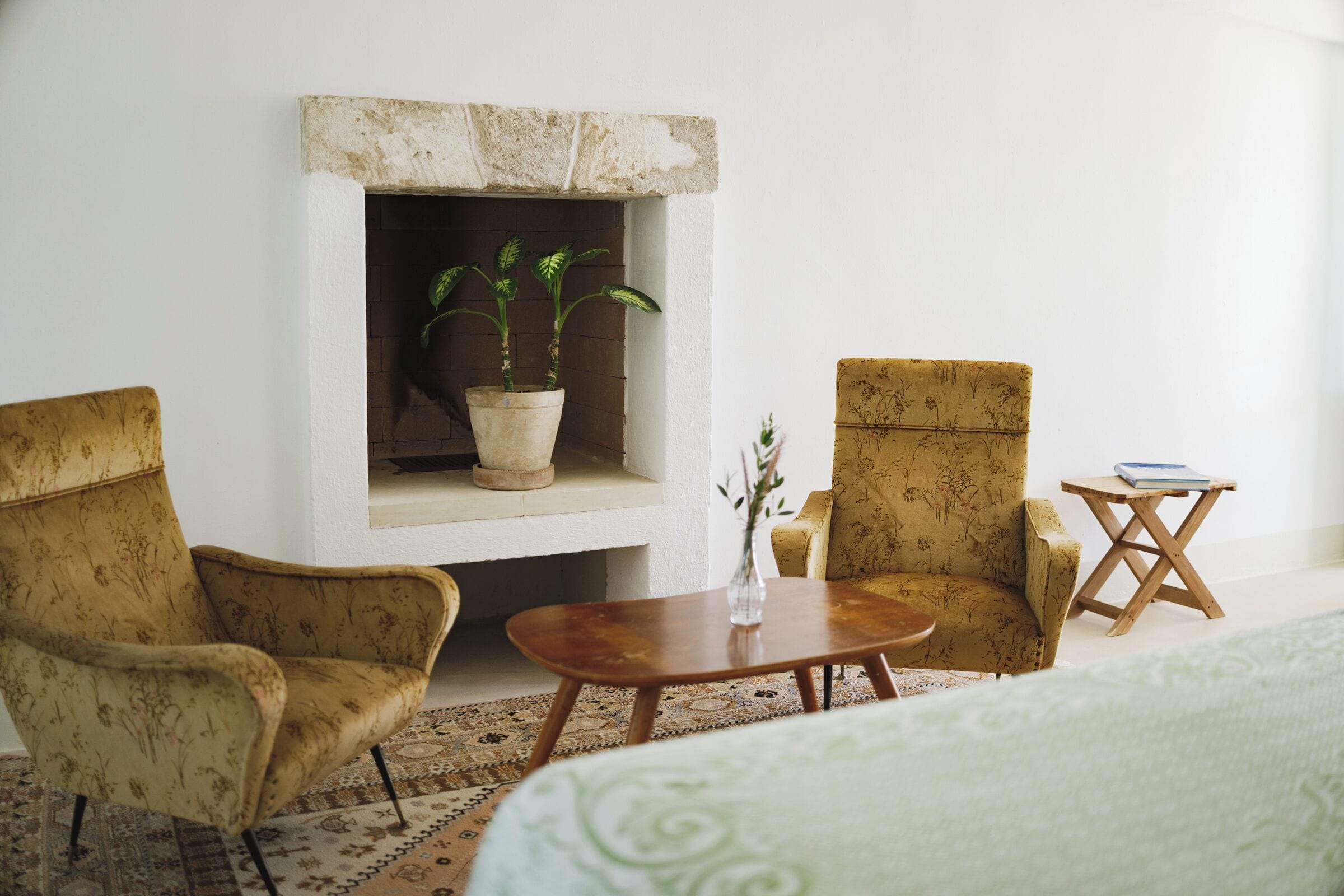 Quarto com lareira, duas poltronas, uma mesa de madeira pequena e um vaso com planta.